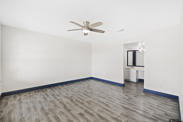 spare room with visible vents, ceiling fan, a sink, wood finished floors, and baseboards