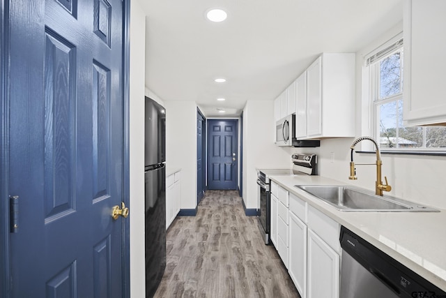 kitchen with stainless steel appliances, light countertops, white cabinets, a sink, and light wood-type flooring