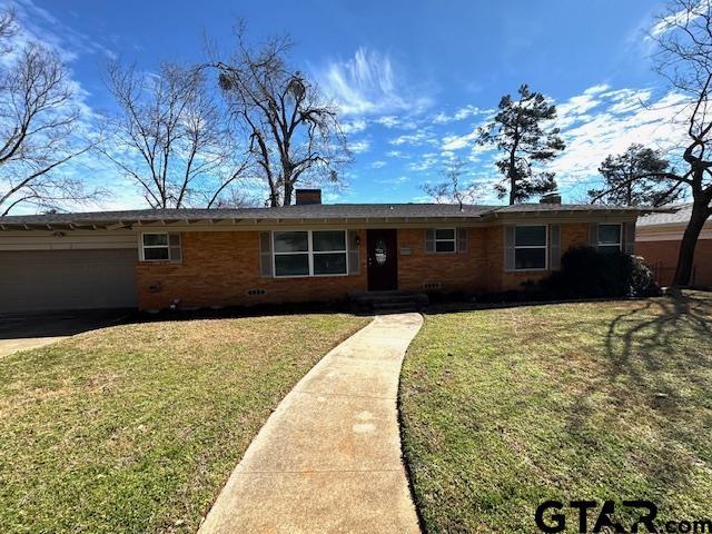 ranch-style home with a front lawn, a chimney, an attached garage, and brick siding