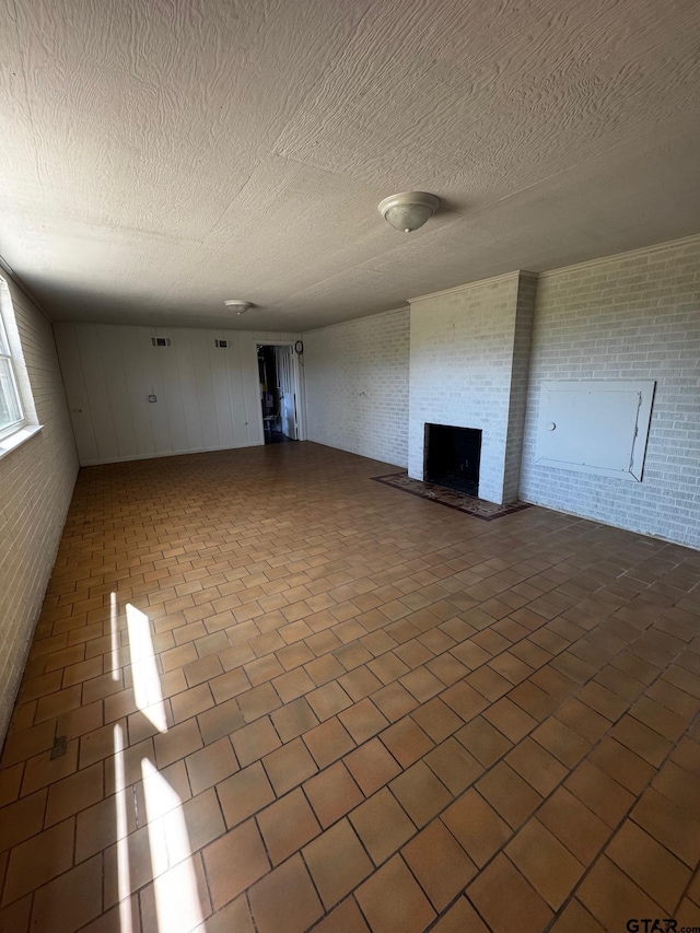 spare room featuring a fireplace, visible vents, a textured ceiling, brick wall, and dark tile patterned floors