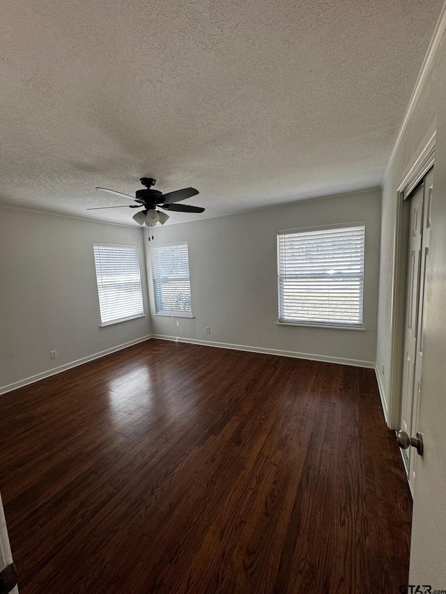 unfurnished room featuring a textured ceiling, dark wood-type flooring, a ceiling fan, and baseboards