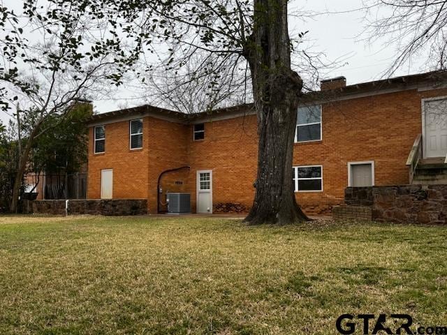 back of property with a chimney, central AC unit, a lawn, and brick siding