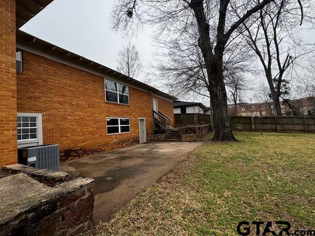 view of side of property with cooling unit, brick siding, fence, a yard, and a patio area