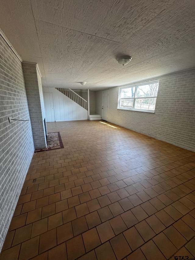 spare room featuring a textured ceiling, brick wall, and brick floor