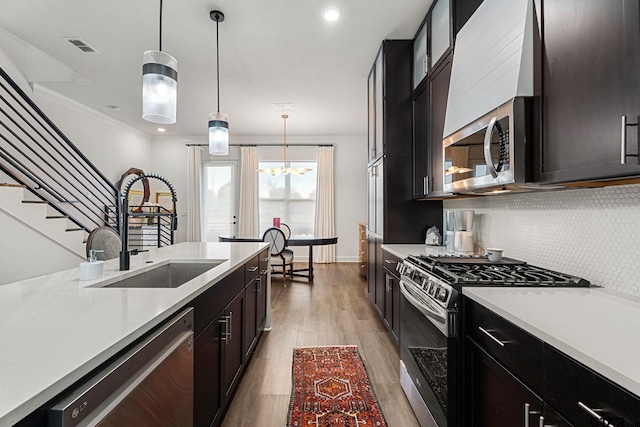 kitchen with sink, stainless steel appliances, light hardwood / wood-style flooring, pendant lighting, and ornamental molding