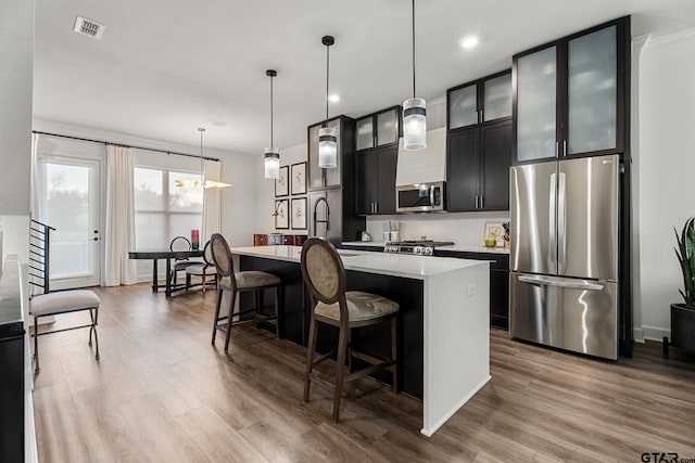 kitchen featuring decorative light fixtures, a kitchen island with sink, appliances with stainless steel finishes, and light hardwood / wood-style flooring