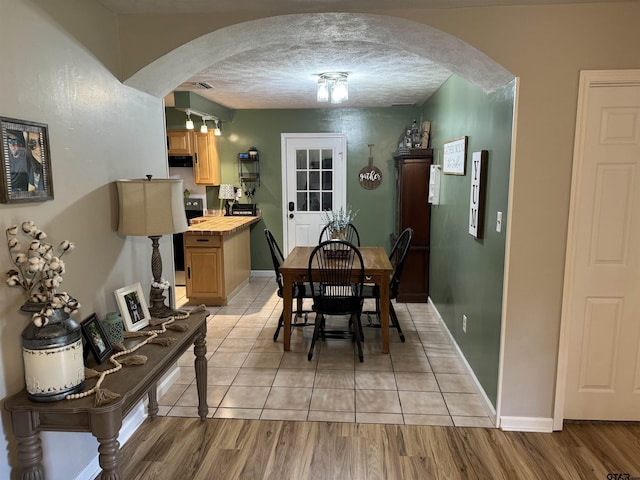 dining area featuring arched walkways, a textured ceiling, baseboards, and light tile patterned floors