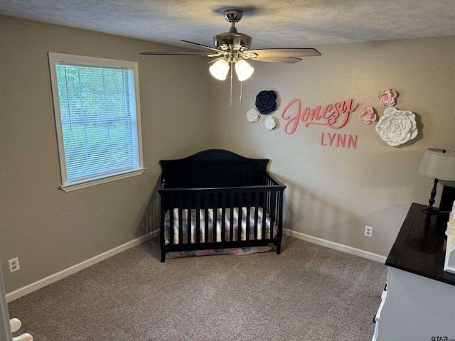 bedroom featuring a nursery area, a textured ceiling, carpet flooring, and ceiling fan