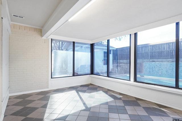 unfurnished room with dark tile patterned flooring, brick wall, and a wealth of natural light