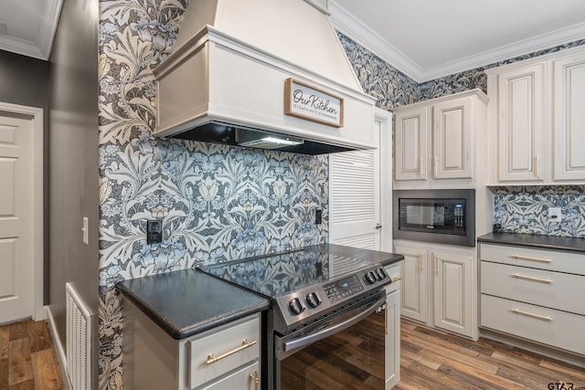 kitchen with black microwave, stainless steel electric range oven, ornamental molding, custom range hood, and light wood-type flooring