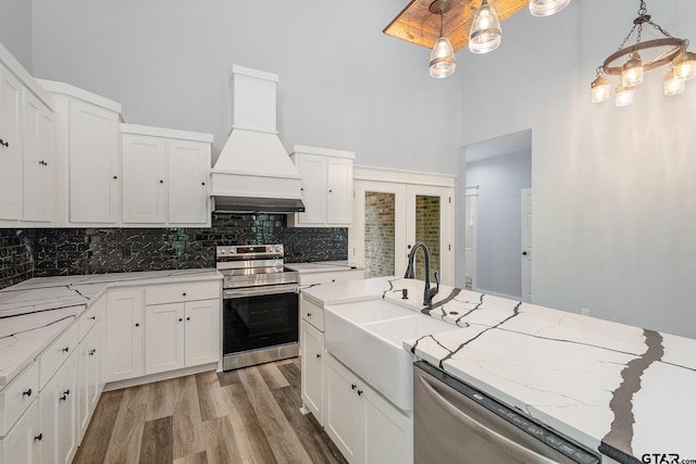 kitchen featuring white cabinetry, decorative light fixtures, premium range hood, and stainless steel appliances