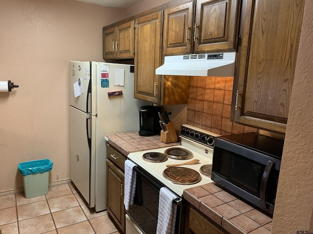 kitchen featuring tile countertops, light tile patterned floors, and white appliances