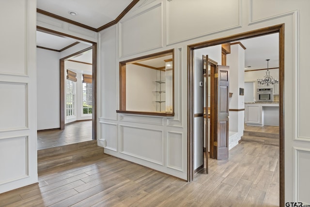 hall with light hardwood / wood-style floors, crown molding, and an inviting chandelier