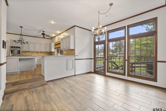 kitchen featuring stainless steel oven, ceiling fan with notable chandelier, tasteful backsplash, white cabinetry, and kitchen peninsula