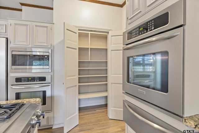 kitchen featuring white cabinets, appliances with stainless steel finishes, light hardwood / wood-style floors, and crown molding