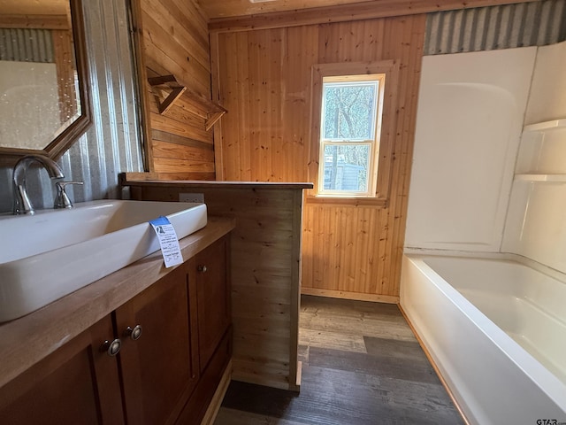 bathroom featuring vanity, wood walls, a bathtub, and wood finished floors