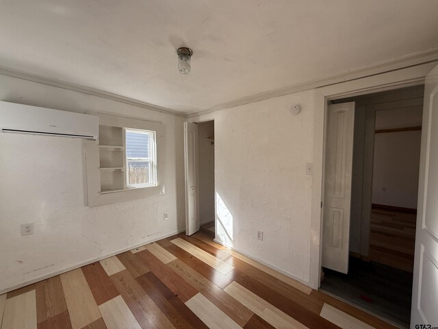 unfurnished bedroom with a wall unit AC, a textured wall, and wood finished floors