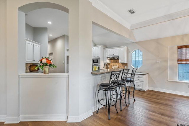 629 Whiteoak Ln, Tyler, TX 75703 - kitchen featuring stainless steel appliances, under cabinet range hood, white cabinets, a kitchen breakfast bar, and backsplash