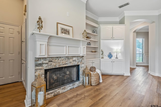 629 Whiteoak Ln, Tyler, TX 75703 - living room featuring light wood-style floors, ornamental molding, a stone fireplace, arched walkways, and built in features