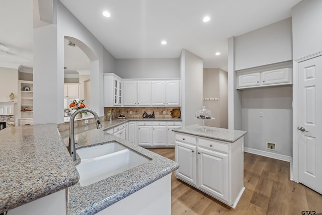 629 Whiteoak Ln, Tyler, TX 75703 - kitchen with light stone countertops, backsplash, light wood finished floors, arched walkways, and white cabinetry