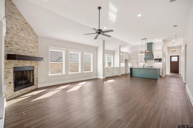 unfurnished living room with a stone fireplace, sink, vaulted ceiling, dark hardwood / wood-style floors, and ceiling fan