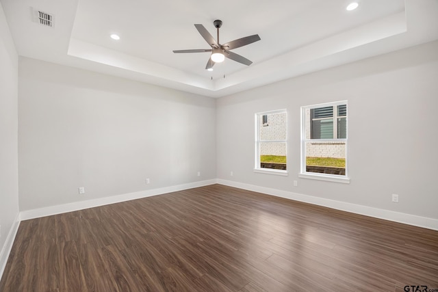 spare room featuring a raised ceiling, ceiling fan, and dark hardwood / wood-style flooring