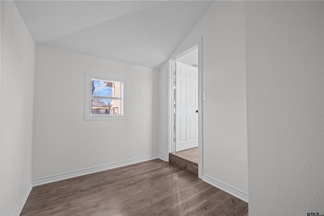 spare room with dark wood-type flooring and lofted ceiling