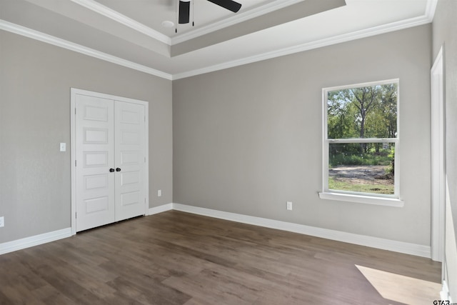 unfurnished bedroom with a closet, crown molding, dark hardwood / wood-style flooring, a tray ceiling, and ceiling fan