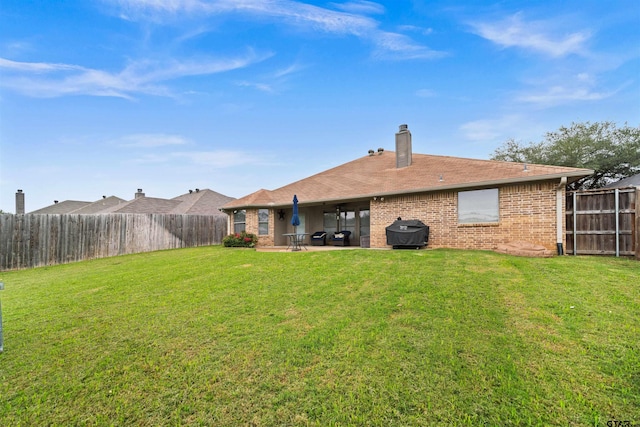 back of property featuring a patio, a fenced backyard, a chimney, a yard, and brick siding