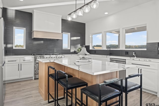 kitchen featuring hanging light fixtures, appliances with stainless steel finishes, a kitchen island, white cabinetry, and a breakfast bar area