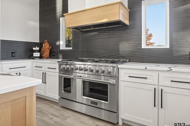 kitchen with light wood-type flooring, tasteful backsplash, custom exhaust hood, double oven range, and white cabinets