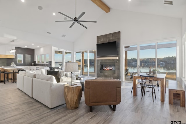 living room featuring beamed ceiling, ceiling fan, high vaulted ceiling, and a tiled fireplace