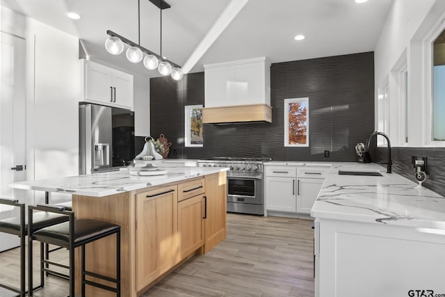 kitchen with a center island, stainless steel appliances, light stone counters, premium range hood, and white cabinets