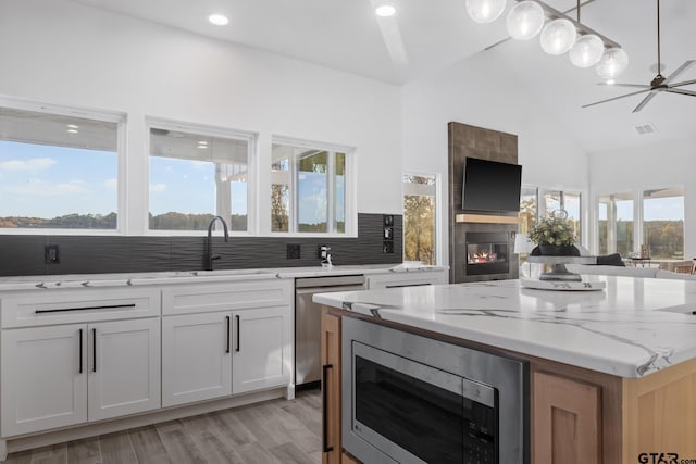 kitchen featuring tasteful backsplash, light stone counters, stainless steel appliances, white cabinetry, and a tiled fireplace