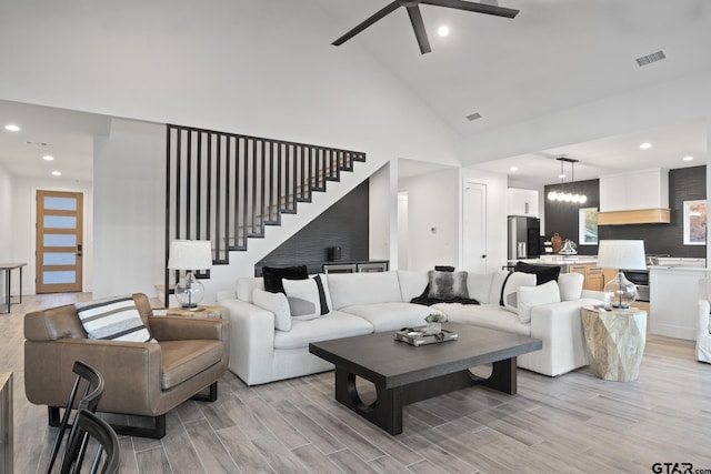 living room featuring light hardwood / wood-style flooring, high vaulted ceiling, and ceiling fan with notable chandelier