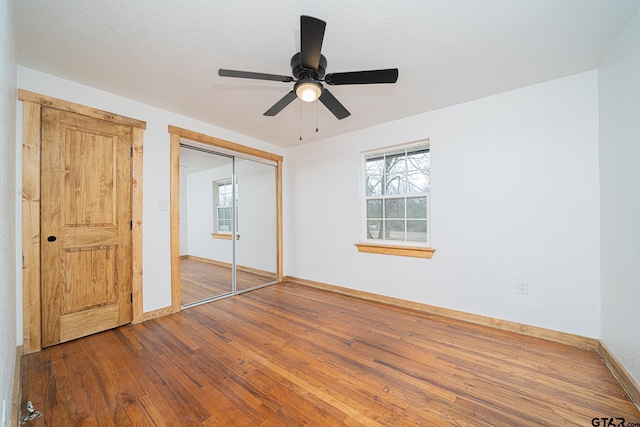 unfurnished bedroom with multiple windows, wood-type flooring, a closet, and ceiling fan