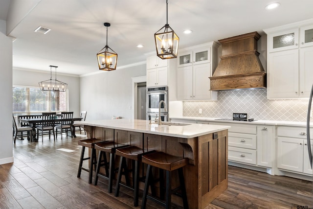 kitchen featuring pendant lighting, a kitchen island with sink, custom range hood, and white cabinets