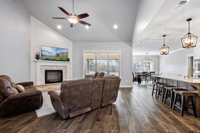 living room featuring dark hardwood / wood-style flooring, a stone fireplace, ceiling fan with notable chandelier, and high vaulted ceiling