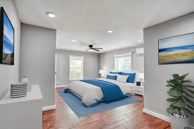 bedroom featuring multiple windows, a wall unit AC, hardwood / wood-style floors, and ceiling fan