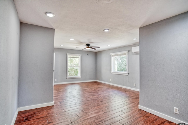 unfurnished room with a textured ceiling, hardwood / wood-style floors, ceiling fan, and an AC wall unit