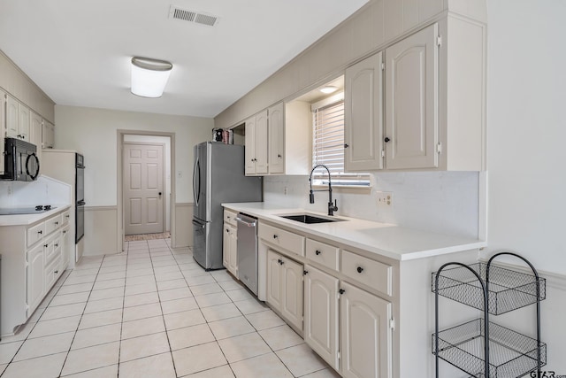 kitchen featuring decorative backsplash, sink, light tile patterned flooring, white cabinets, and black appliances