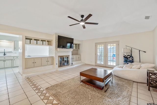 tiled living room featuring ceiling fan, a fireplace, french doors, and sink