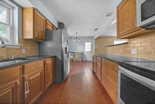 17607 Kristopher Cir, Whitehouse, TX 75791 - kitchen featuring stainless steel appliances, brown cabinets, a chandelier, dark wood finished floors, and backsplash