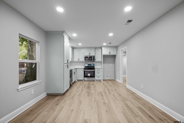 kitchen with backsplash, white cabinetry, light hardwood / wood-style flooring, and appliances with stainless steel finishes