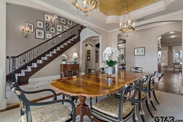 dining room featuring arched walkways, a raised ceiling, a notable chandelier, and ornamental molding