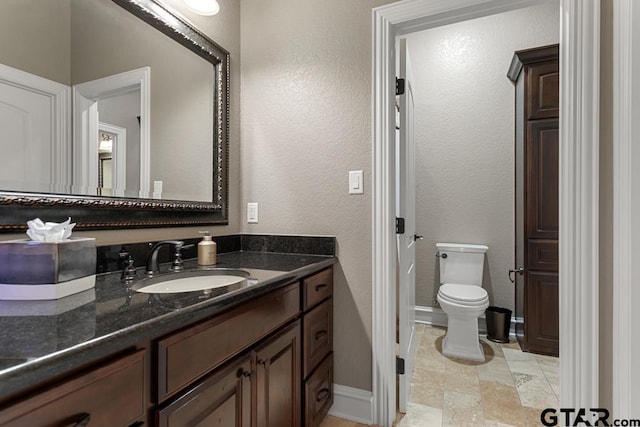 bathroom with toilet, a textured wall, baseboards, and vanity