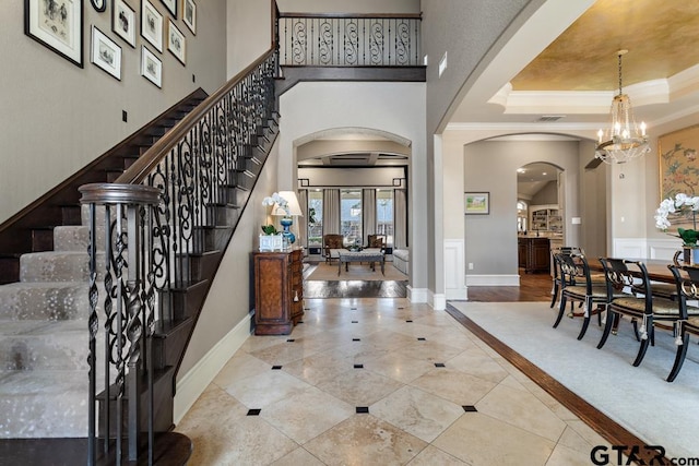 tiled entryway with arched walkways, a raised ceiling, ornamental molding, stairs, and a notable chandelier