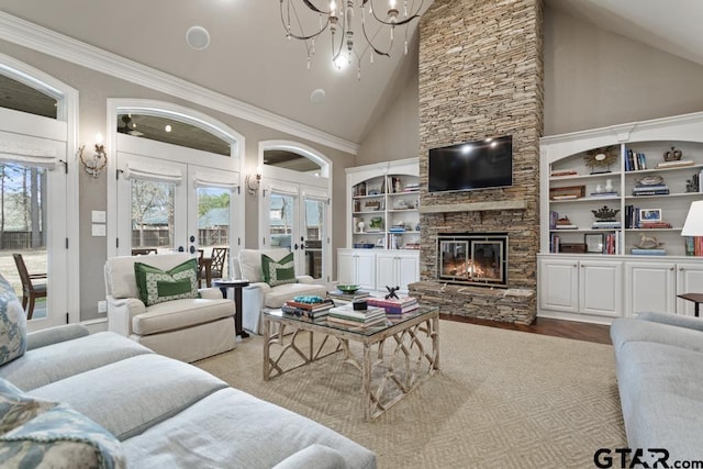 living area featuring high vaulted ceiling, a stone fireplace, wood finished floors, french doors, and an inviting chandelier