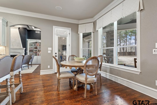 dining space with baseboards, arched walkways, dark wood-style flooring, crown molding, and a fireplace