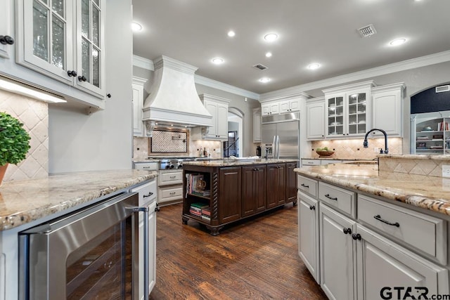 kitchen with crown molding, custom exhaust hood, stainless steel built in refrigerator, a sink, and beverage cooler